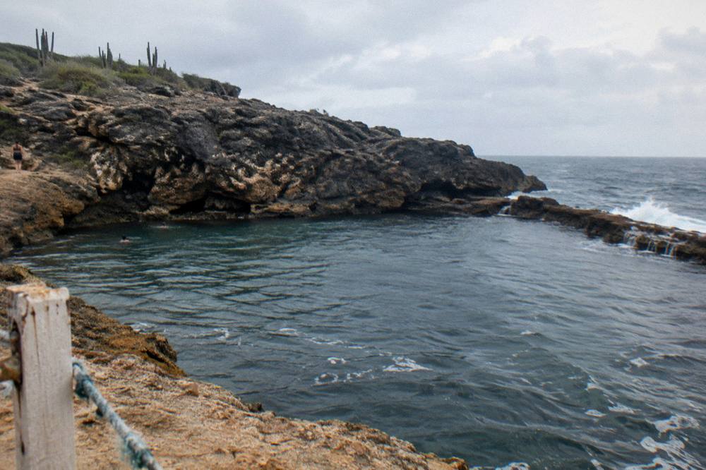 A quiet volcanic rock pool at the base of coastal cliffs with gentle waves beyond the rim