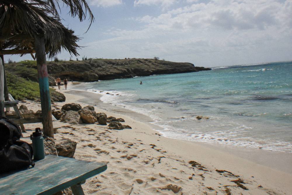 Pale sand curving along calm turquoise shallows under scattered clouds