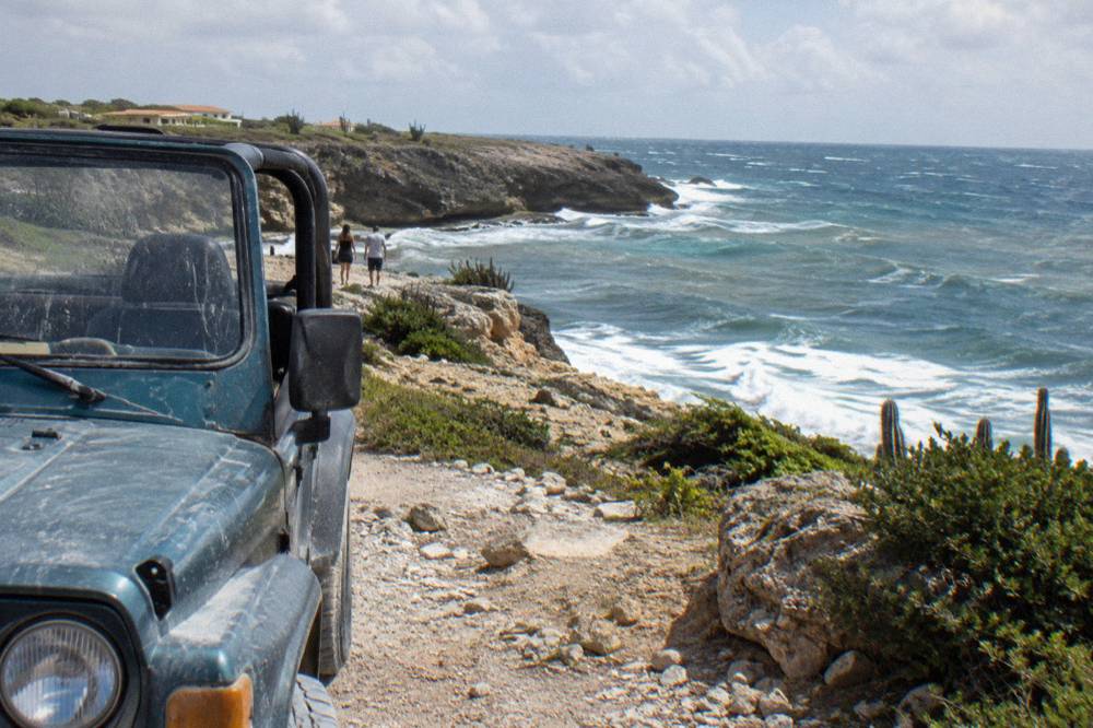 An open-air four wheel drive vehicle parked on a rocky desert track near coastal cliffs