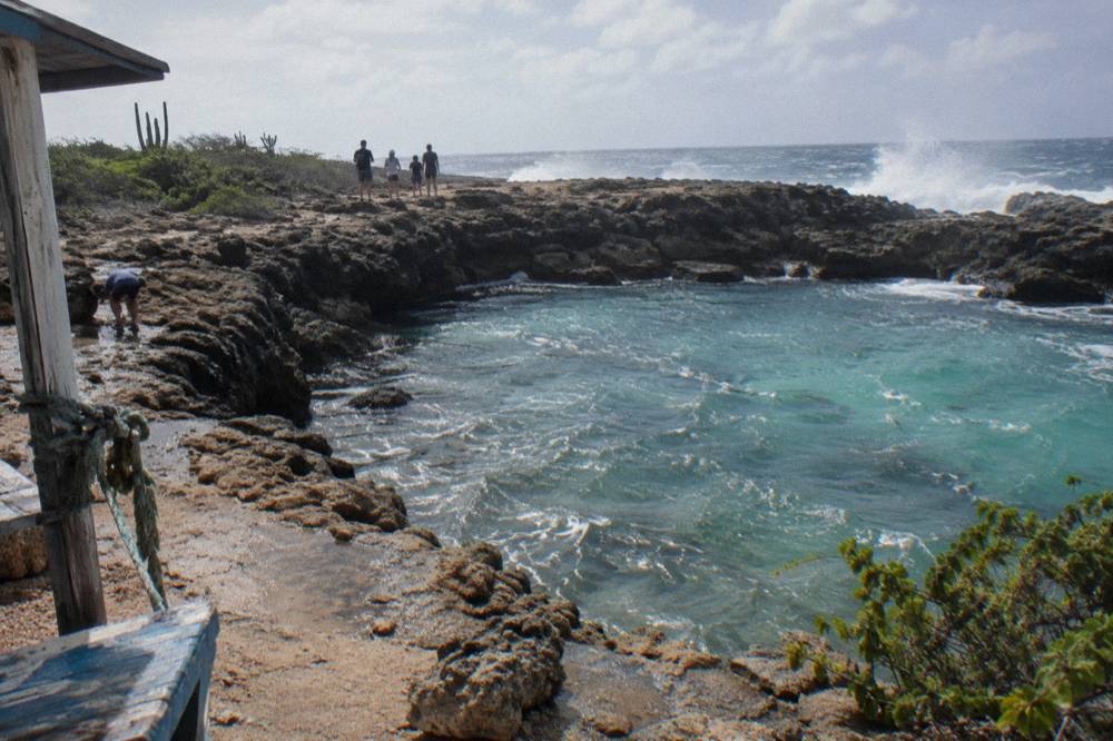 A small guided walking group pausing on a coastal trail above turquoise water in a rock basin