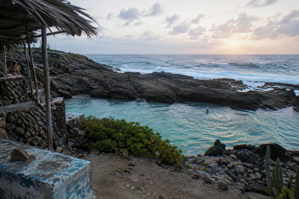 First light over a calm volcanic rock pool with gentle surf beyond the rim