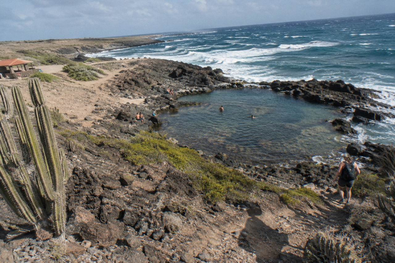 Rocky desert trail descending toward a volcanic rock pool on Aruba's northeast coast