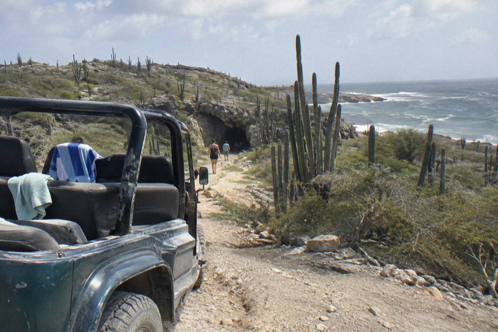 An open four wheel drive jeep parked on a rough dirt track in dry parkland near the coast