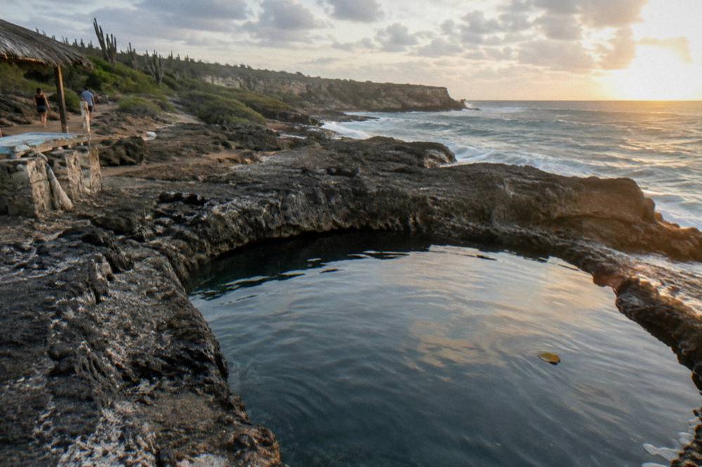 Calm turquoise natural pool basin surrounded by dark volcanic rock at sunrise