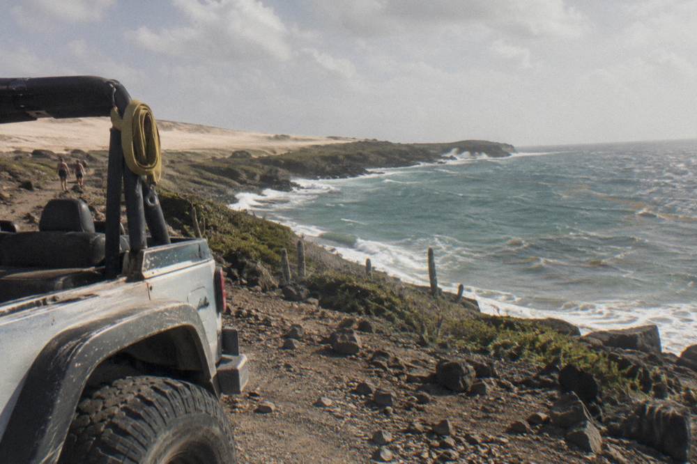 Open-air four-wheel-drive vehicle on a rocky trail above the sea