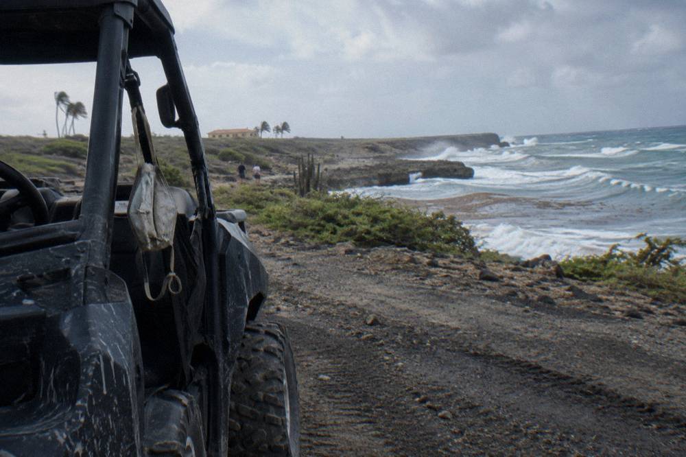 Four-wheeled vehicle parked on a coastal dirt road with waves beyond
