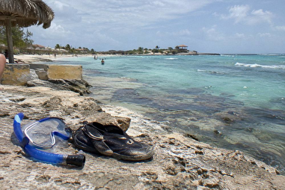 Snorkel mask and water shoes resting on dry volcanic rock beside calm water