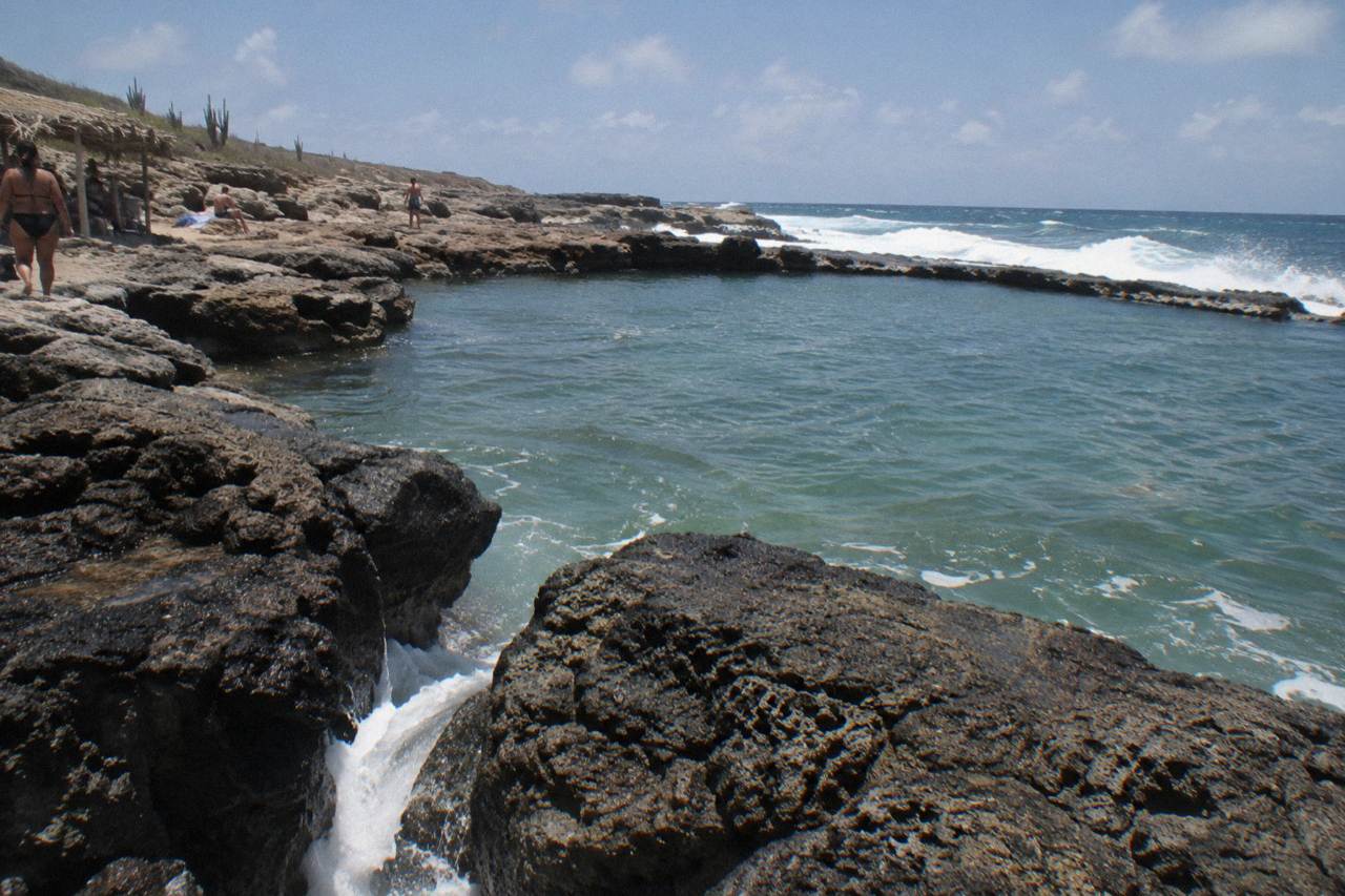 Volcanic rock rim enclosing a calm natural pool with waves breaking beyond it on a rocky coast