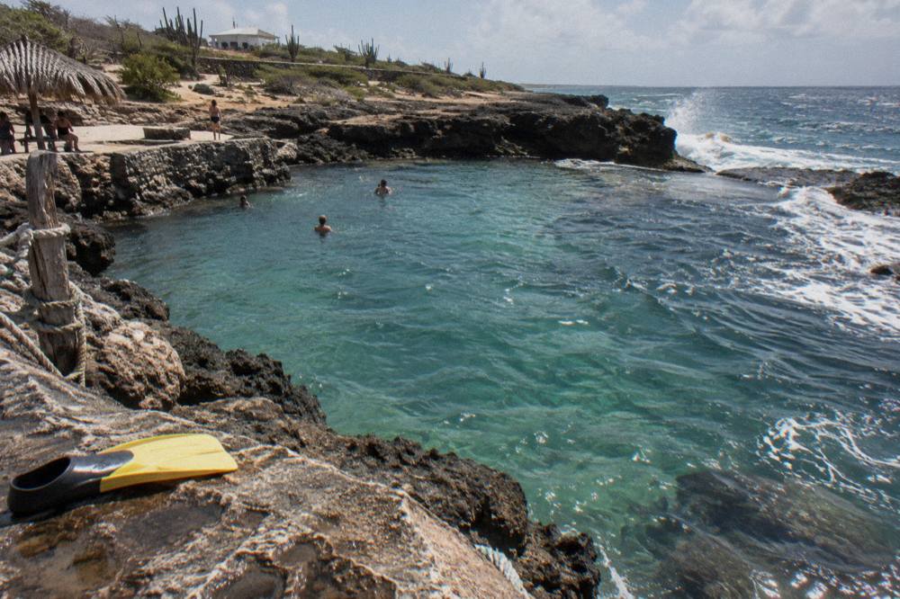Turquoise water pooled inside dark volcanic rock with white spray breaking on the outer rim