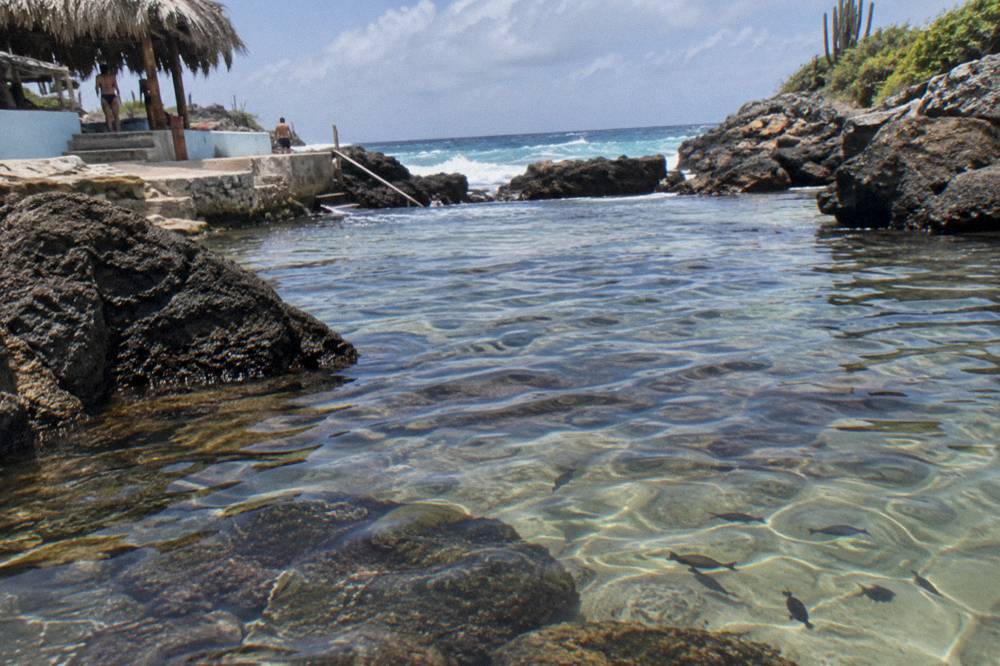 Shallow clear water over smooth dark rocks inside a sheltered natural pool