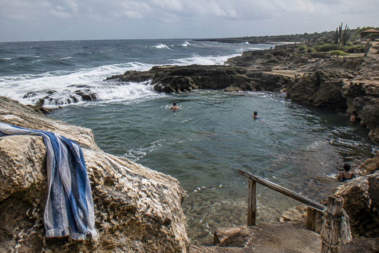 A natural rock pool on a volcanic coastline with waves breaking on the outer rim under an open sky