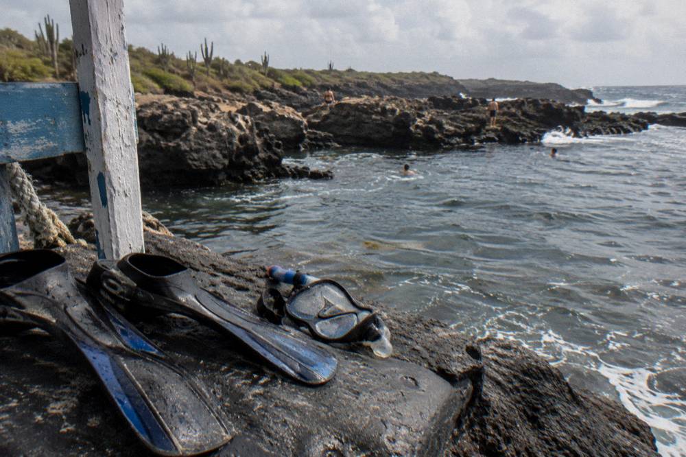 Snorkel mask and fins resting on dark volcanic rock beside still water