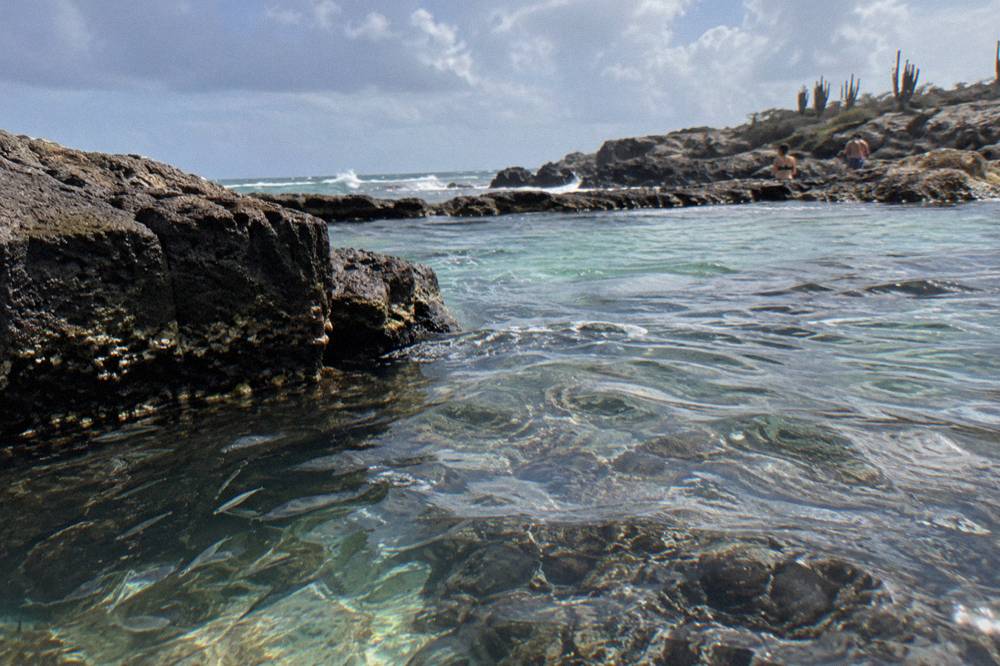 A sheltered natural pool basin with clear shallow water enclosed by dark volcanic rock