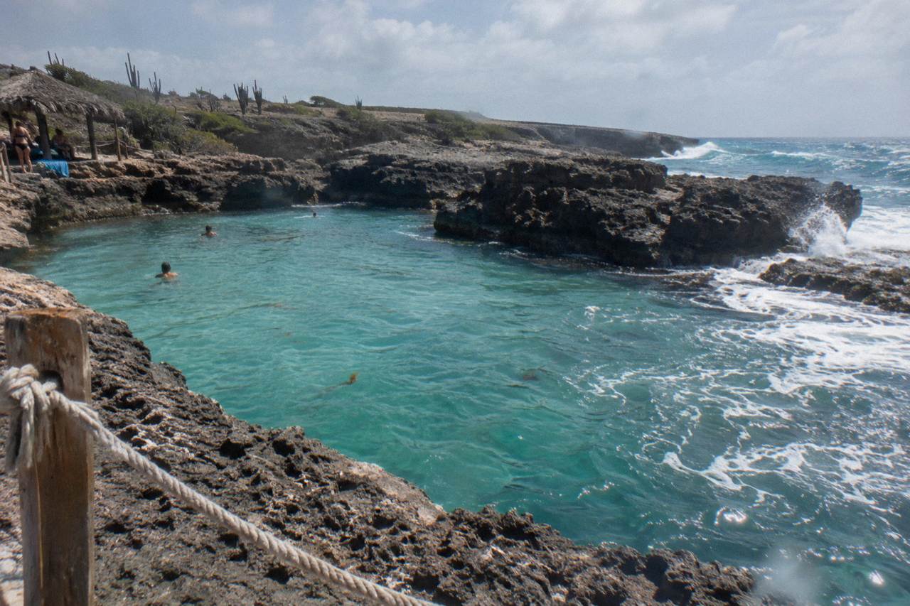 Clear turquoise water in a volcanic rock pool on Aruba's north-east coast with waves breaking on the outer rocks