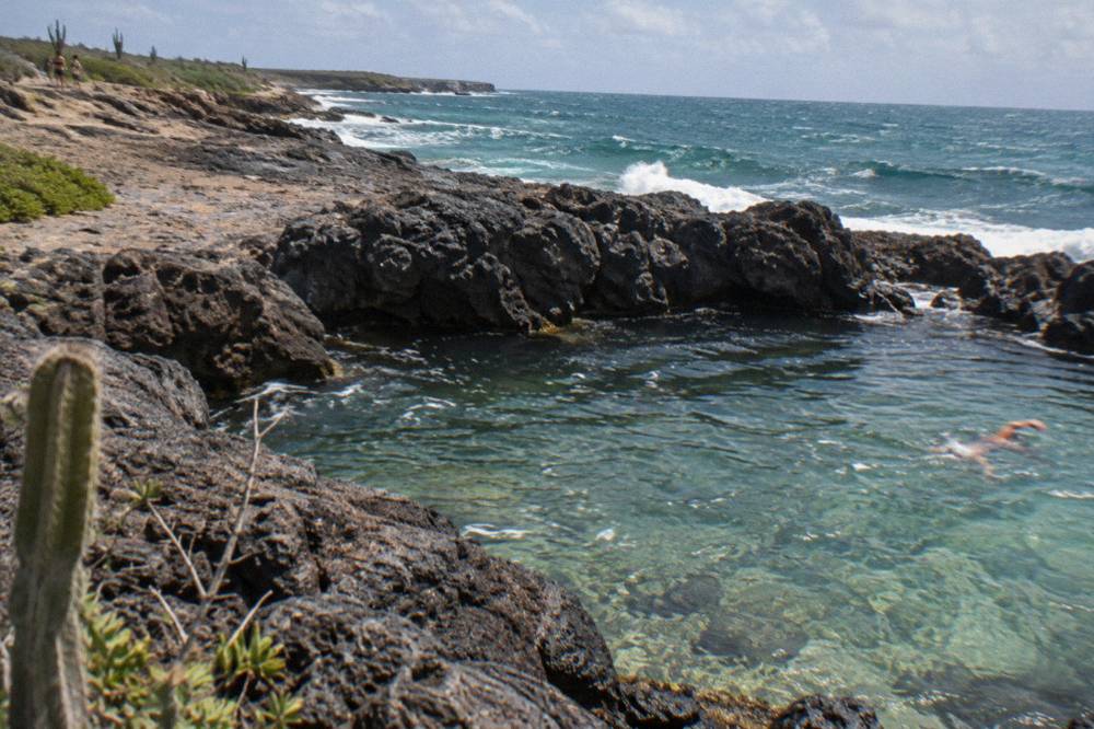 Dark volcanic rocks forming a natural basin with clear shallow water