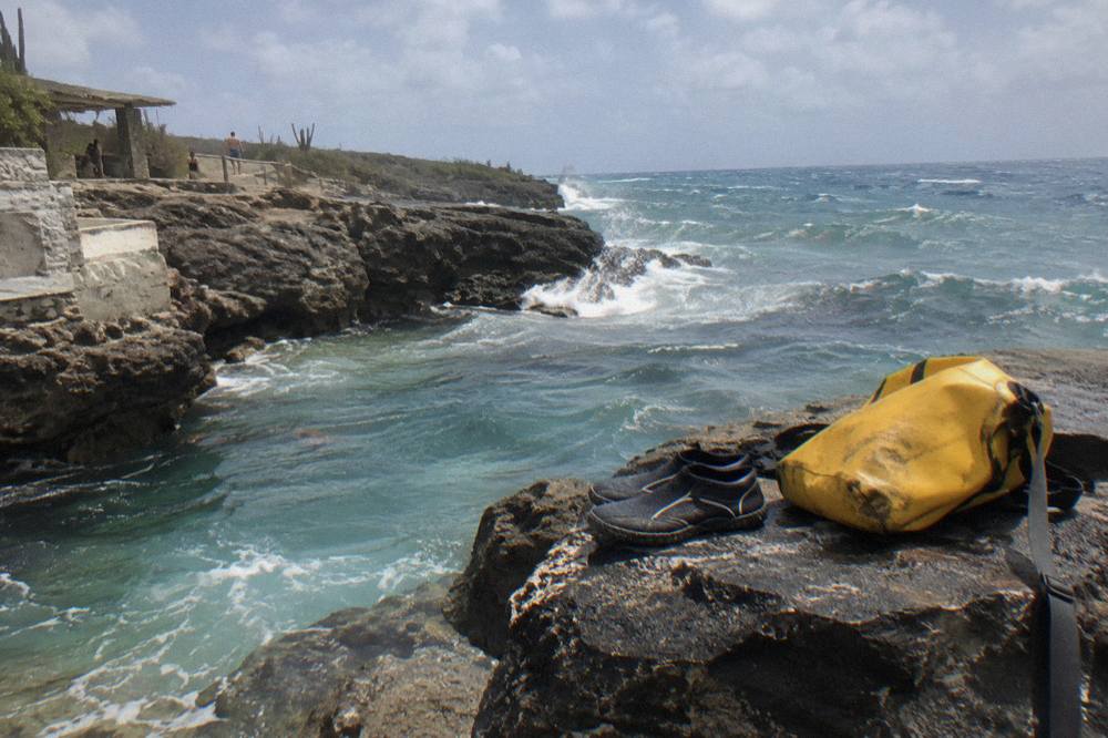 Water shoes and a dry bag set on volcanic rock beside a natural pool