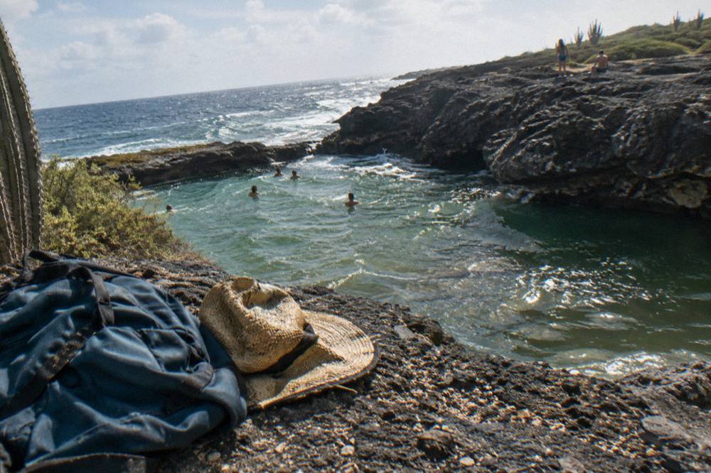 A packed day bag and hat resting on a rock ledge above a natural pool